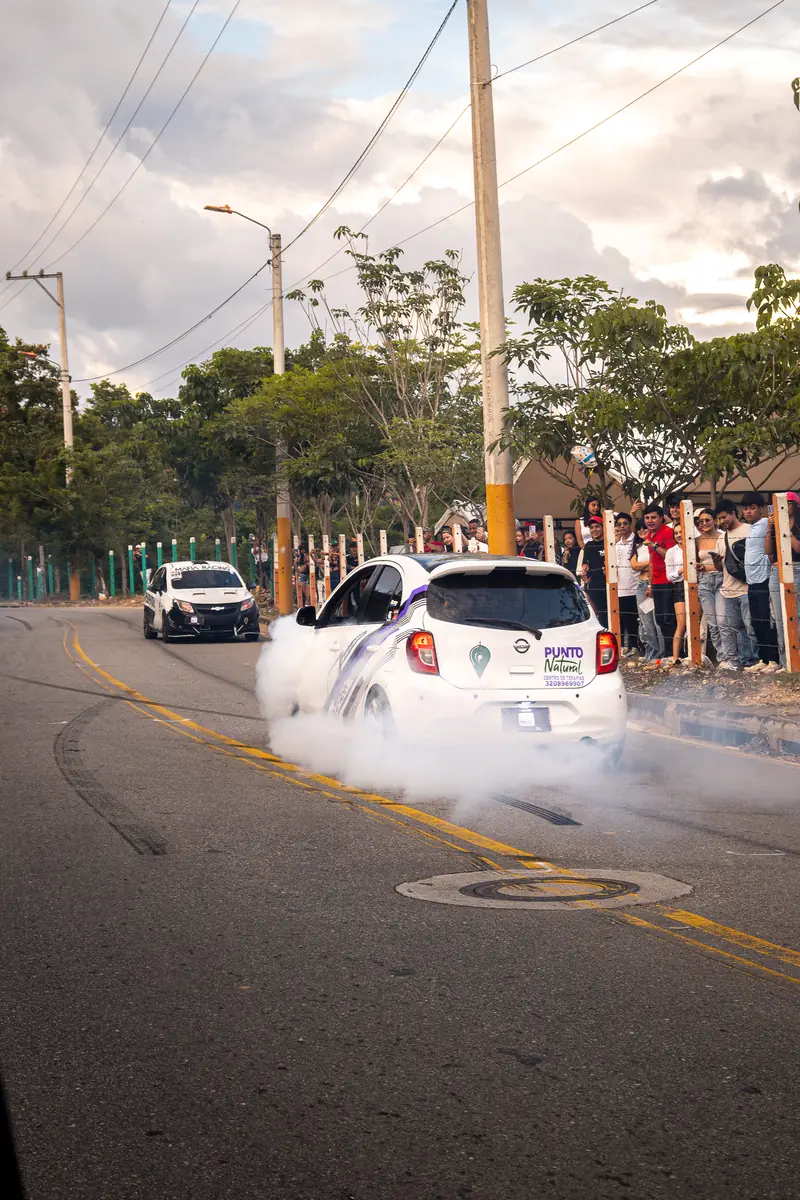 Carro blanco quemando llanta frente al público, envuelto en humo